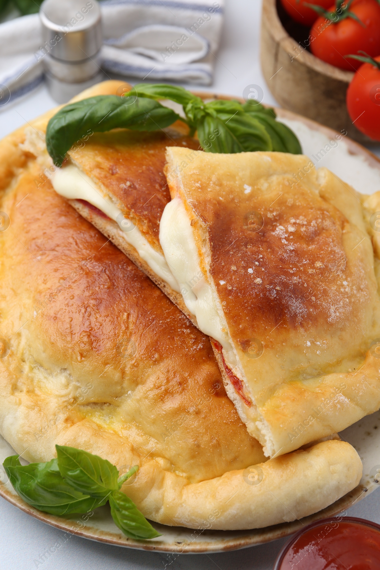 Photo of Pieces of delicious calzone pizza with mozzarella, tomatoes and basil on white table, closeup