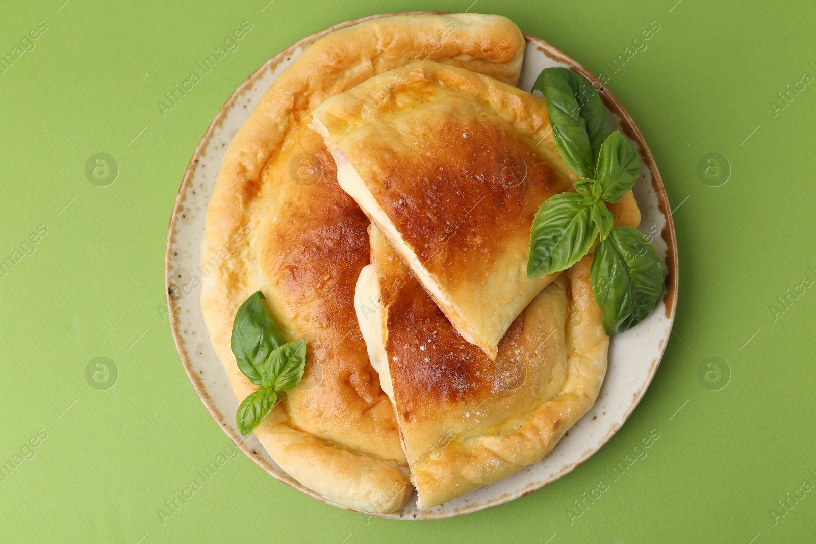 Photo of Pieces of delicious calzone pizza with mozzarella, tomatoes and basil on green background, top view