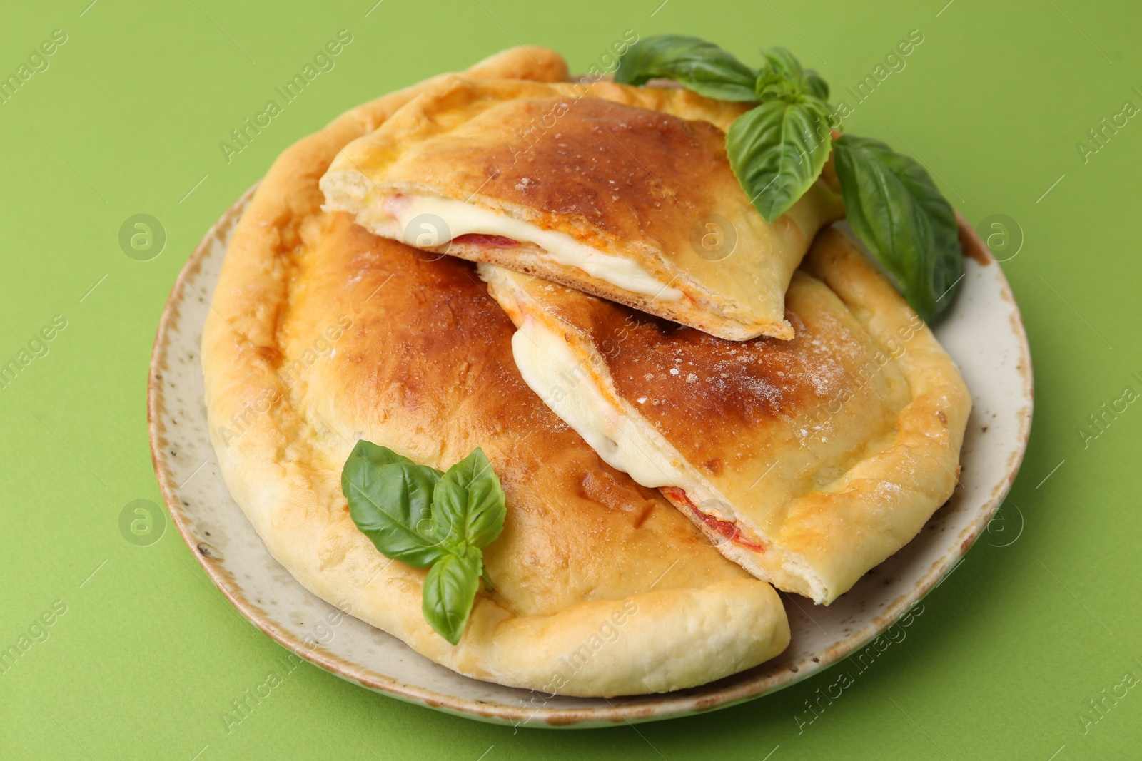 Photo of Pieces of delicious calzone pizza with mozzarella, tomatoes and basil on green background, closeup