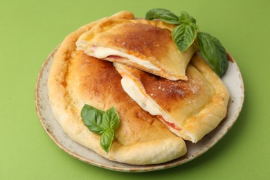 Pieces of delicious calzone pizza with mozzarella, tomatoes and basil on green background, closeup