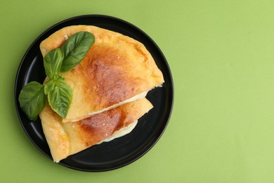 Pieces of delicious calzone pizza with mozzarella, tomatoes and basil on green background, top view. Space for text