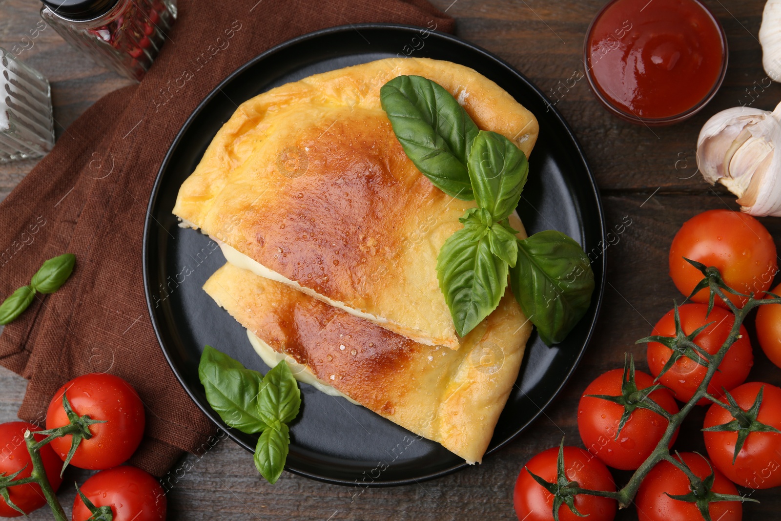 Photo of Pieces of delicious calzone pizza with mozzarella, tomatoes and basil on wooden table, flat lay