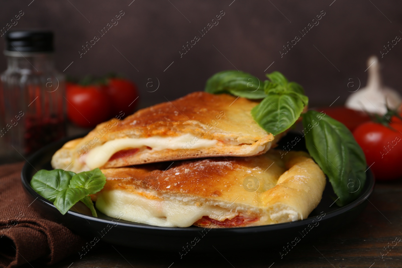 Photo of Pieces of delicious calzone pizza with mozzarella, tomatoes and basil on wooden table, closeup