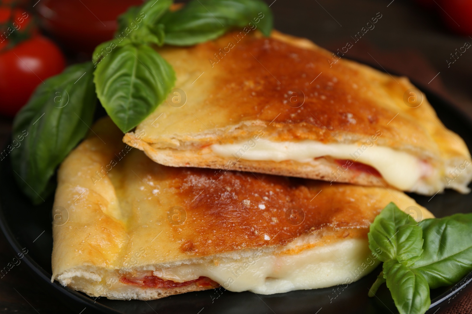 Photo of Pieces of delicious calzone pizza with mozzarella, tomatoes and basil on table, closeup