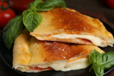 Pieces of delicious calzone pizza with mozzarella, tomatoes and basil on table, closeup