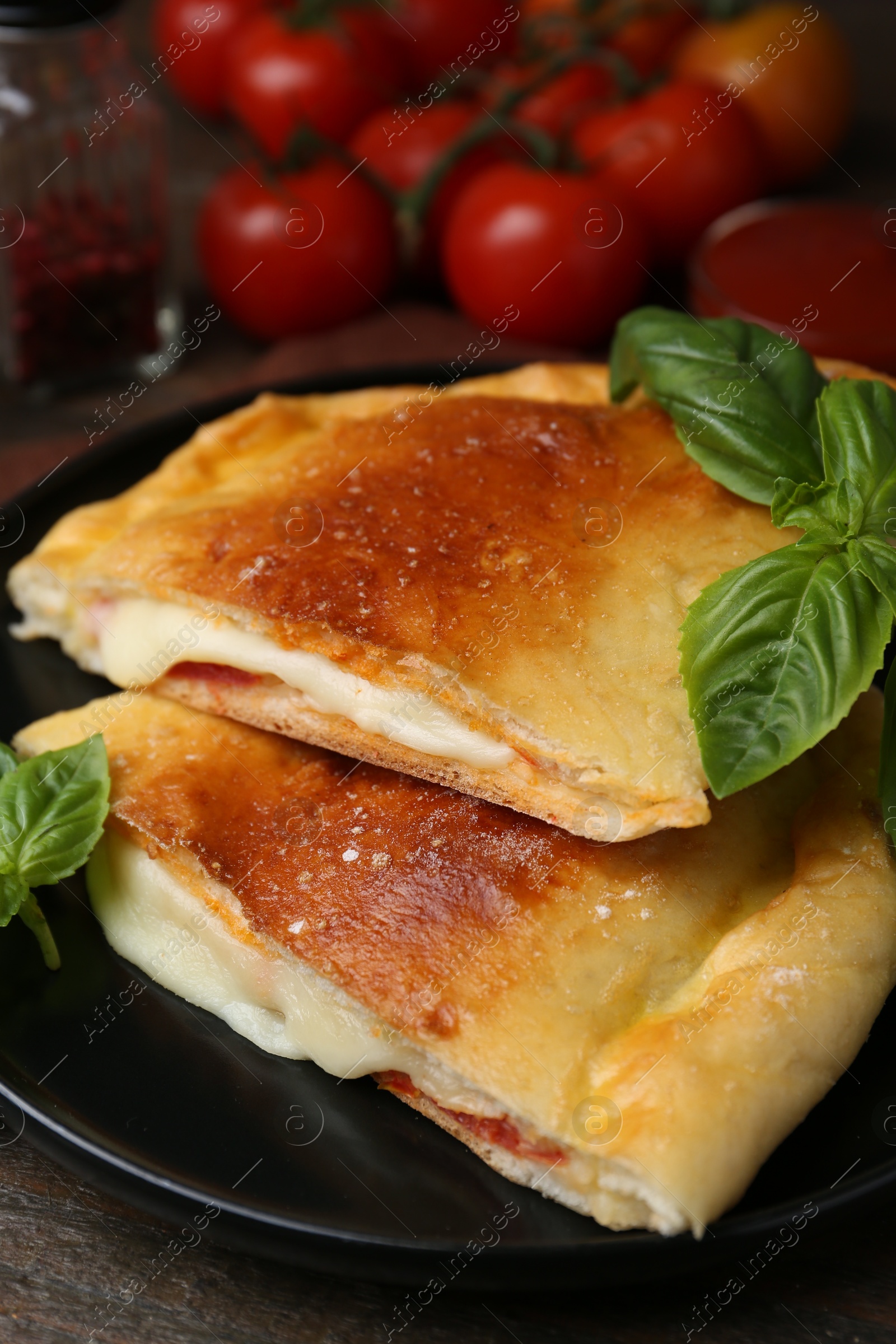 Photo of Pieces of delicious calzone pizza with mozzarella, tomatoes and basil on wooden table, closeup