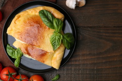 Photo of Pieces of delicious calzone pizza with mozzarella, tomatoes and basil on wooden table, flat lay. Space for text