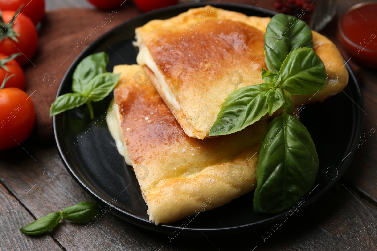 Photo of Pieces of delicious calzone pizza with mozzarella, tomatoes and basil on wooden table, closeup