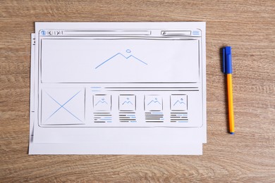 Developing UI design. Sketches of website wireframes and pen on wooden table, top view