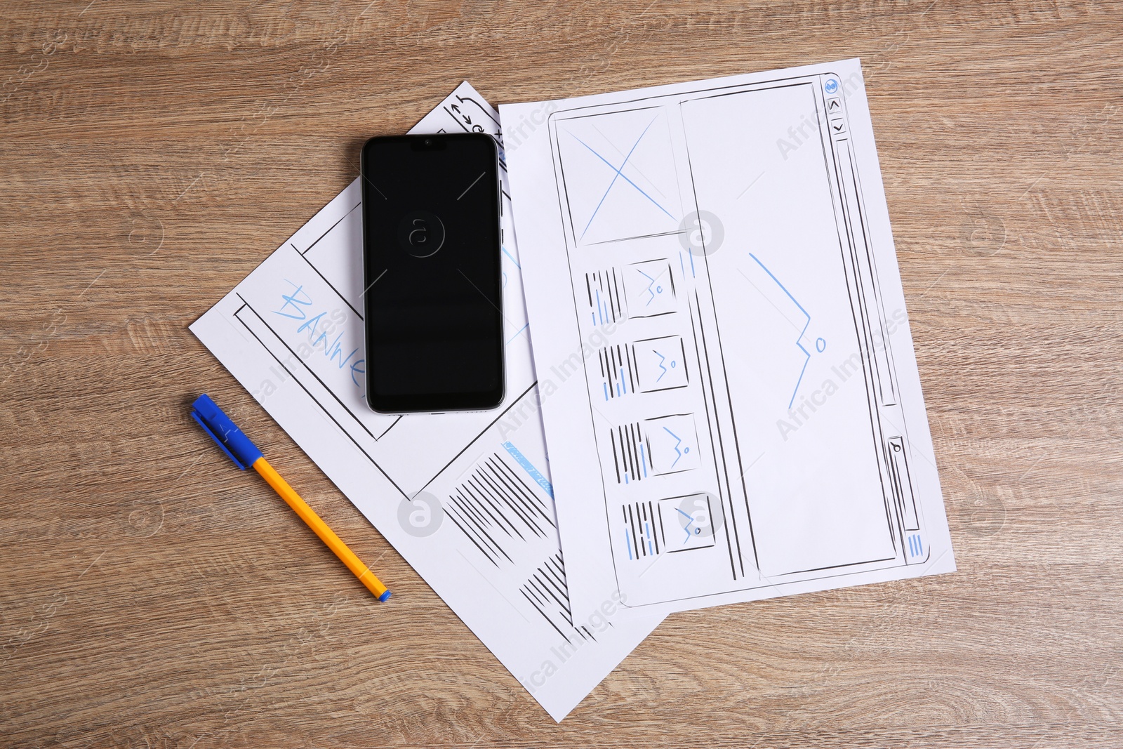 Photo of Developing UI design. Sketches of website wireframes, smartphone and pen on wooden table, top view