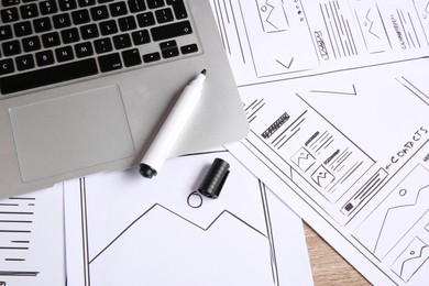 Developing UI design. Sketches of website wireframes, laptop and felt pen on wooden table, above view