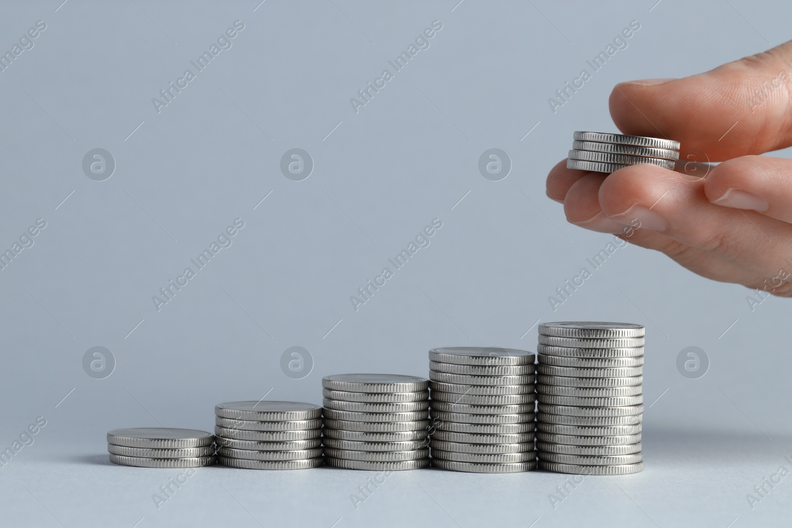 Photo of Salary concept. Woman putting coins on stack against light grey background, closeup