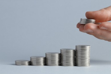 Photo of Salary concept. Woman putting coins on stack against light grey background, closeup