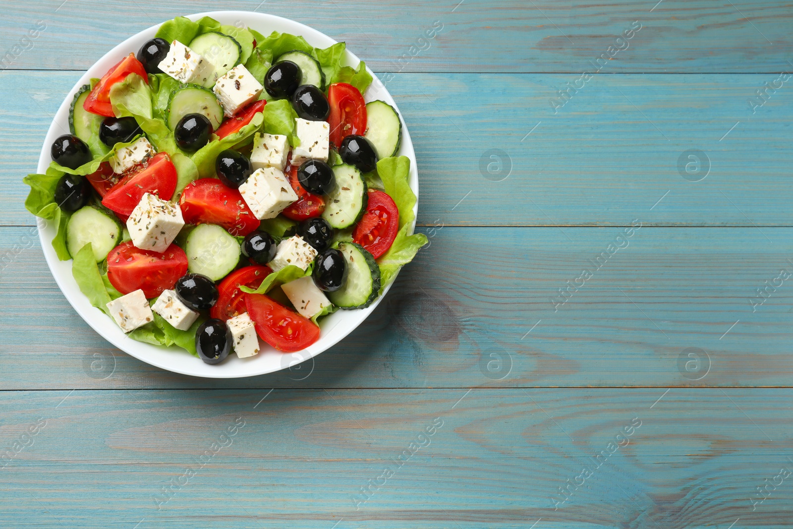 Photo of Delicious salad with feta cheese on light blue wooden table, top view. Space for text