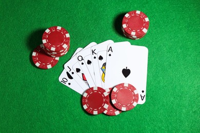 Photo of Playing cards and poker chips on green table, flat lay