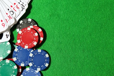 Photo of Playing cards and poker chips on green table, flat lay. Space for text