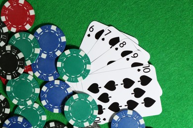 Photo of Playing cards and poker chips on green table, flat lay