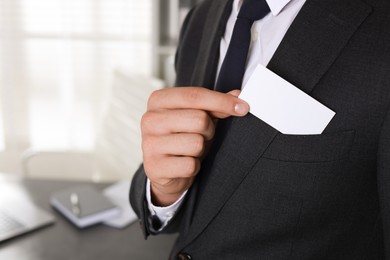 Man taking blank business card from pocket of his jacket in office, closeup. Mockup for design