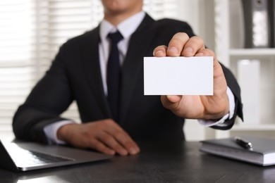 Photo of Man holding blank business card at table in office, closeup. Mockup for design