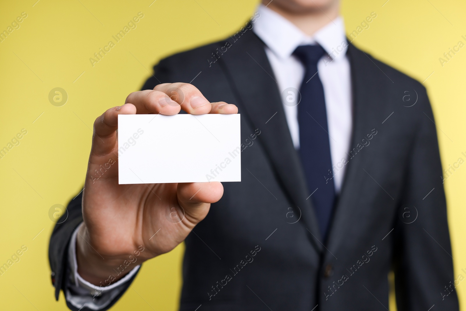 Photo of Man holding blank business card on yellow background, closeup. Mockup for design