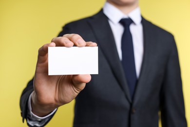 Photo of Man holding blank business card on yellow background, closeup. Mockup for design