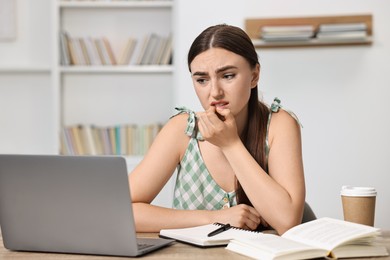 Photo of Tired student preparing for exam with laptop at table indoors