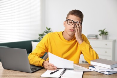 Tired student preparing for exam at table indoors