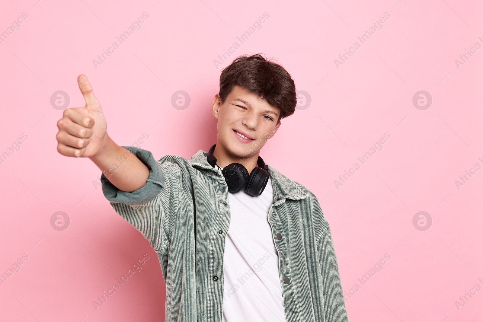 Photo of Teenage boy with headphones showing thumbs up on pink background