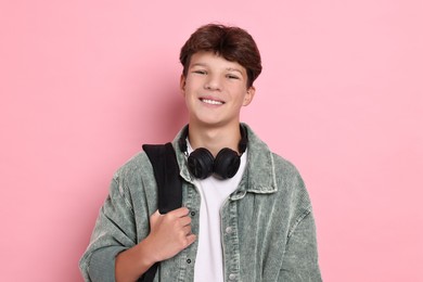 Photo of Happy teenage boy with headphones and backpack on pink background