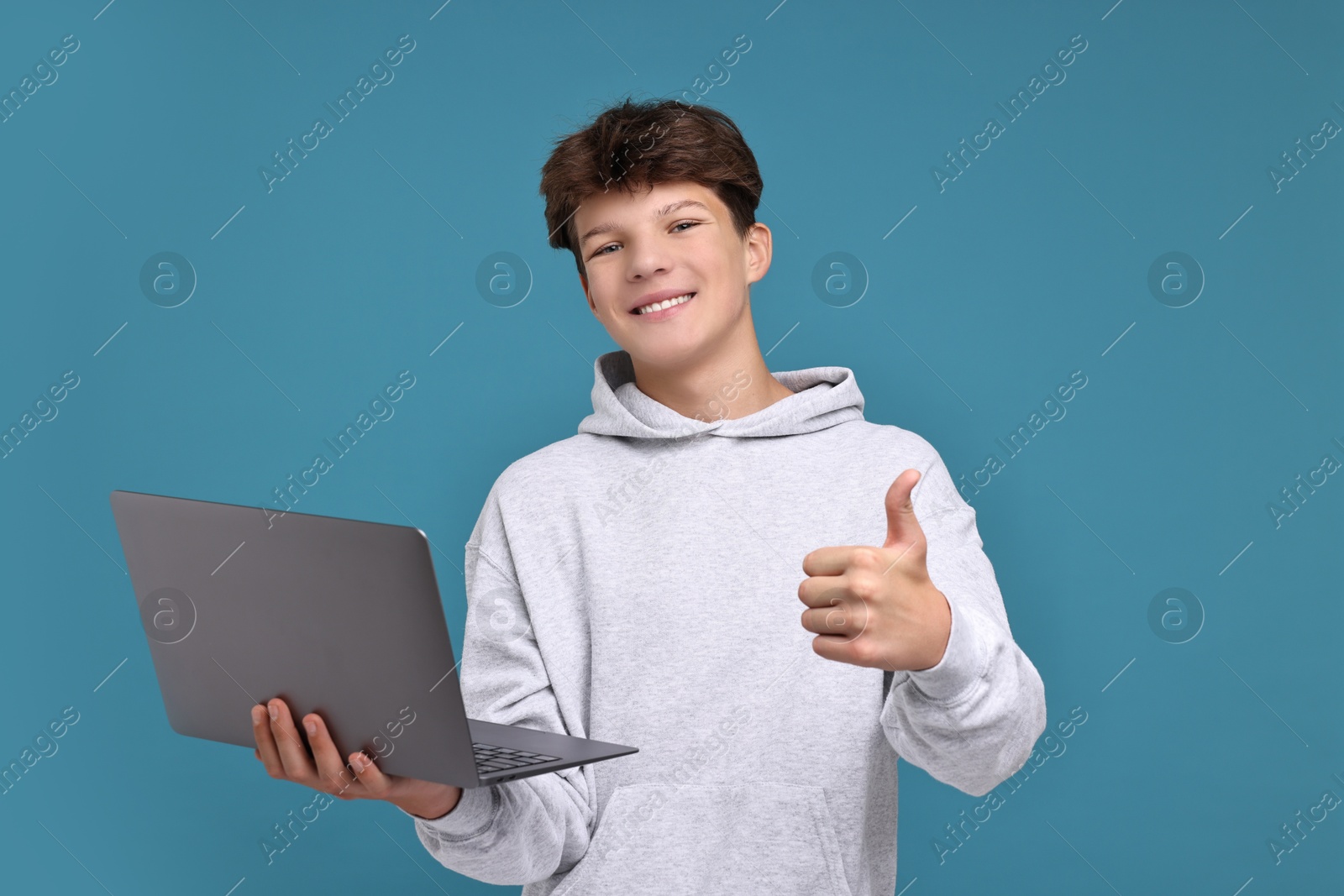 Photo of Teenage boy with laptop showing thumbs up on light blue background