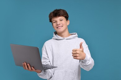 Photo of Teenage boy with laptop showing thumbs up on light blue background