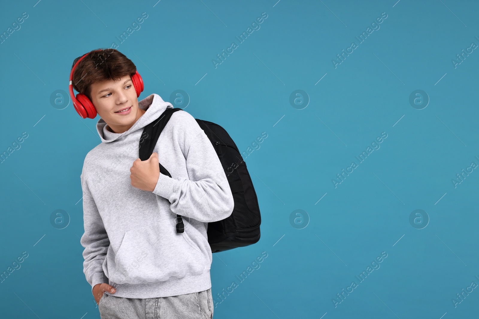 Photo of Teenage boy in headphones with backpack on light blue background, space for text