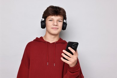 Photo of Teenage boy in headphones with smartphone on light grey background