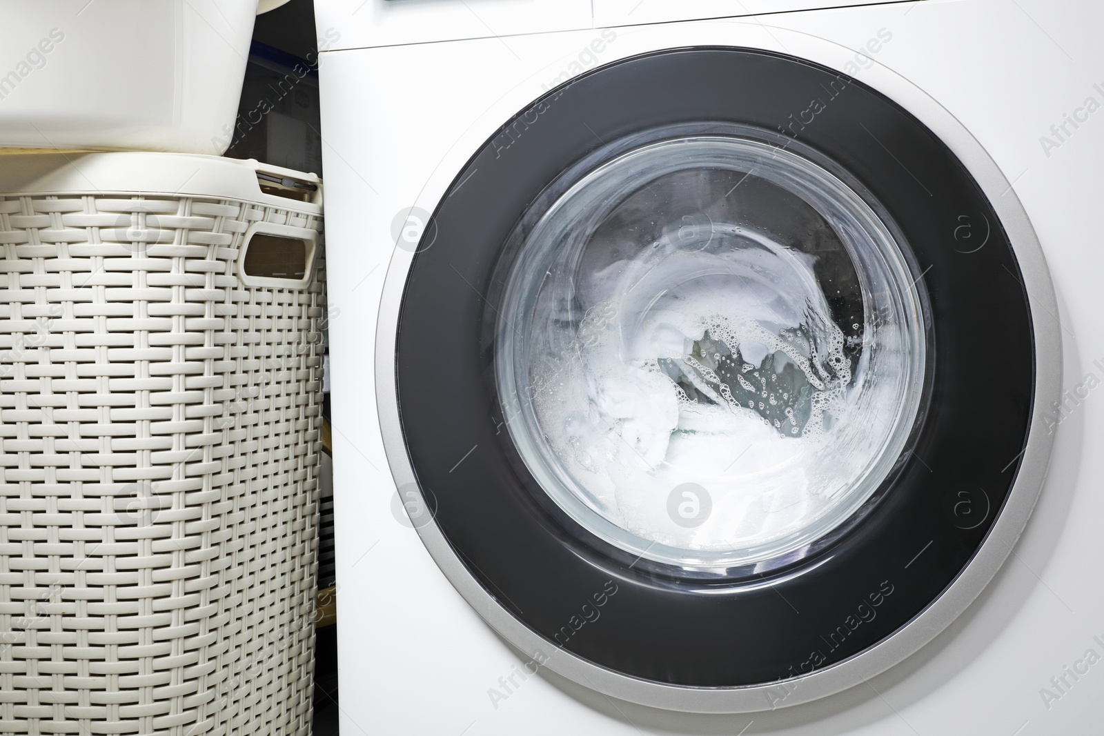 Photo of Washing machine with clothes and suds near laundry basket