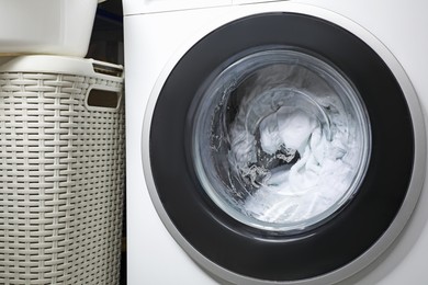 Photo of Washing machine with clothes and suds near laundry basket