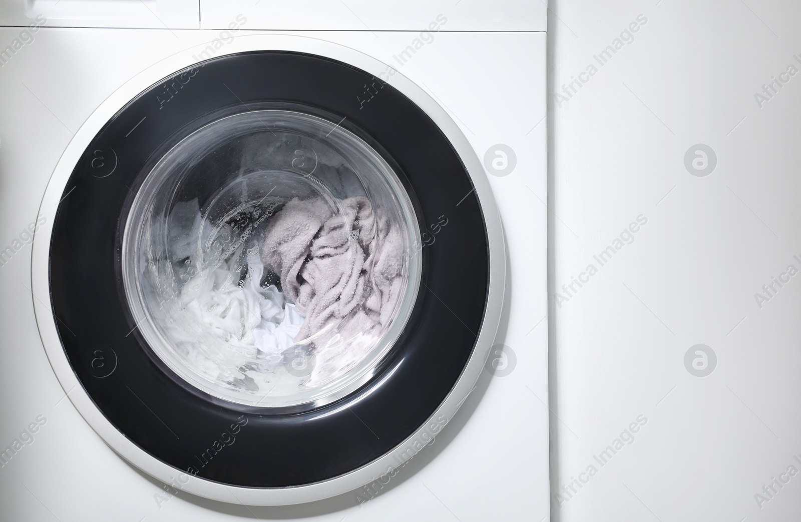 Photo of Washing machine with clothes as background, closeup. Space for text