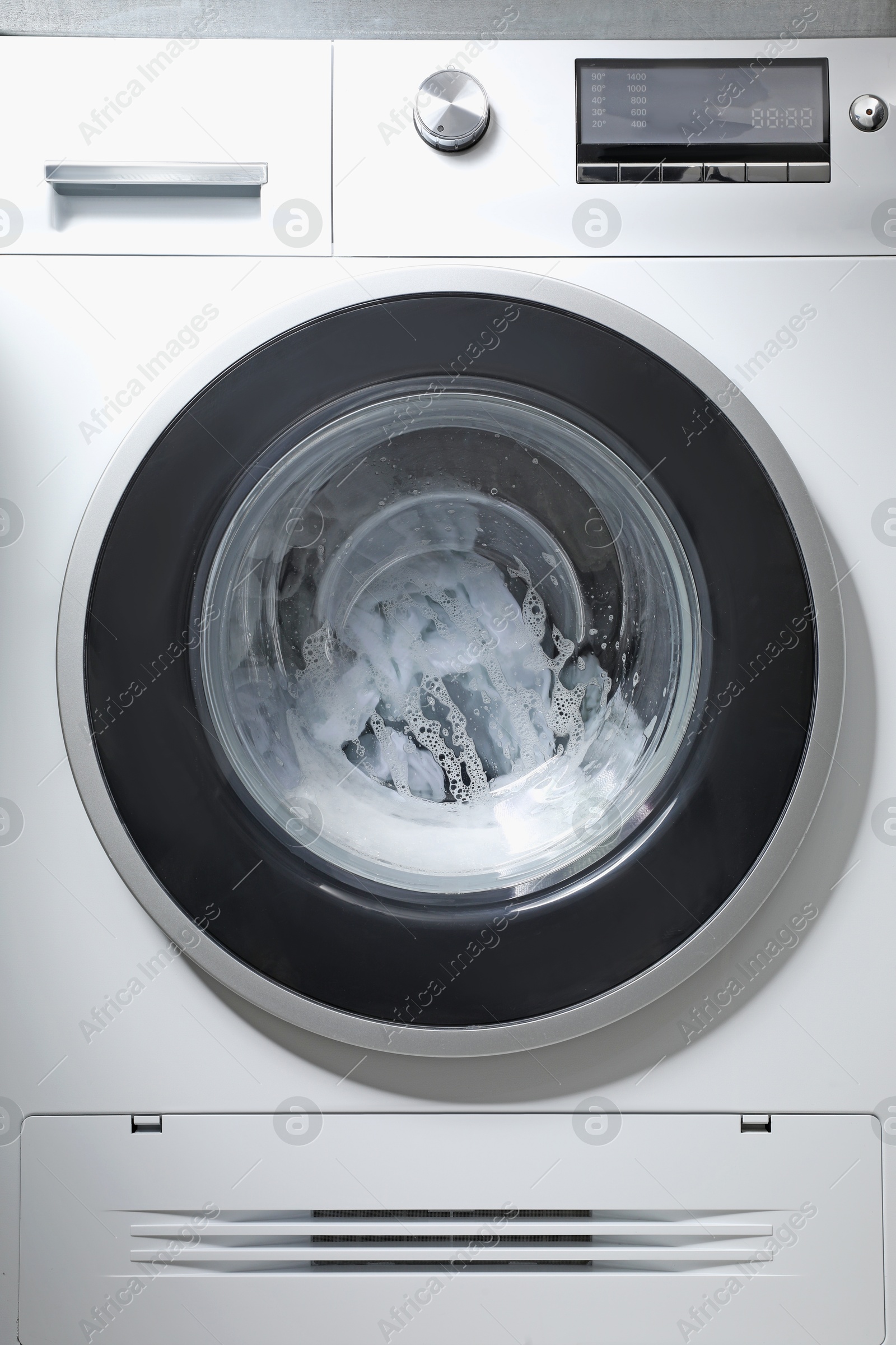 Photo of Washing machine with clothes and suds as background, closeup