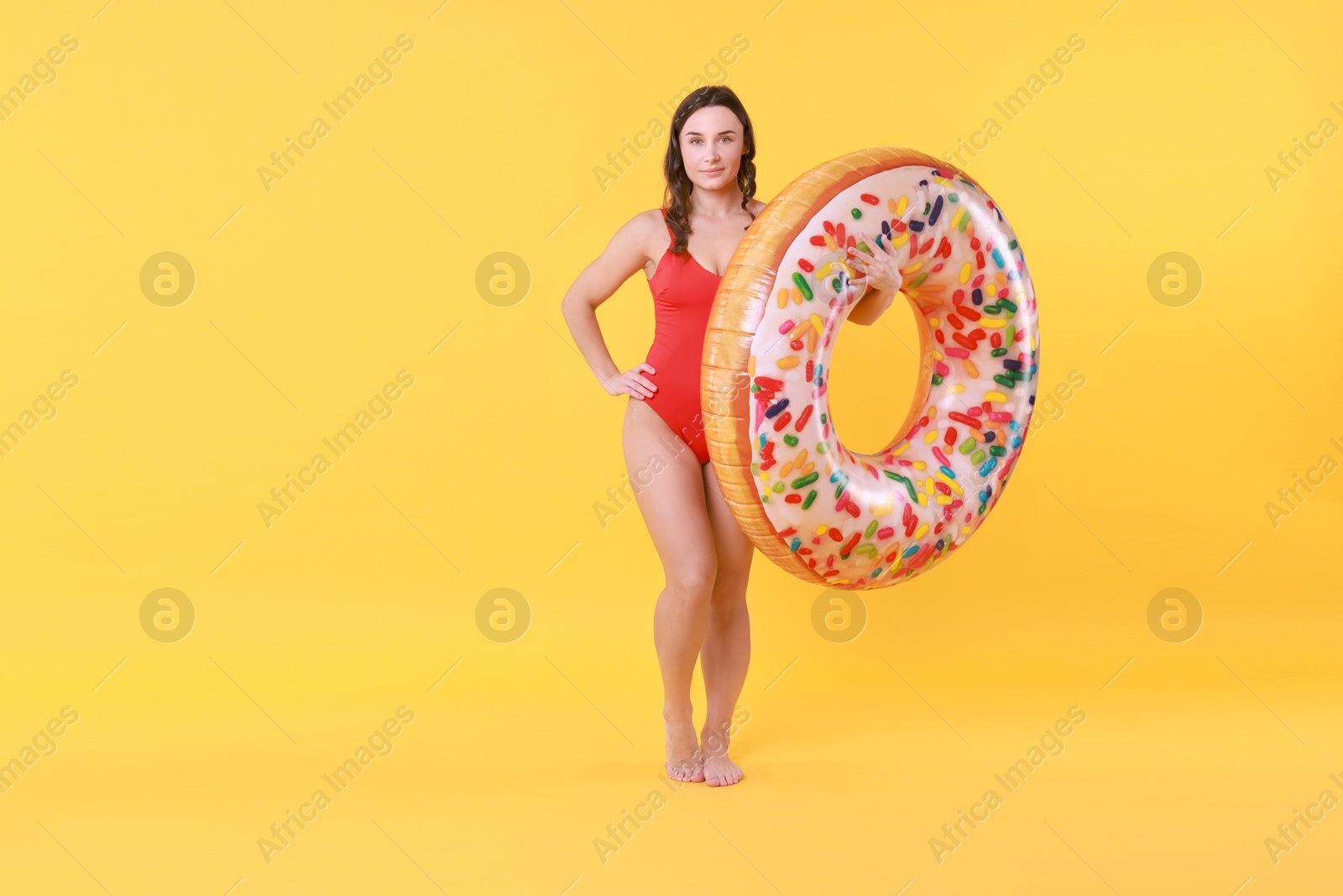 Photo of Beautiful woman in swimsuit with inflatable ring on yellow background