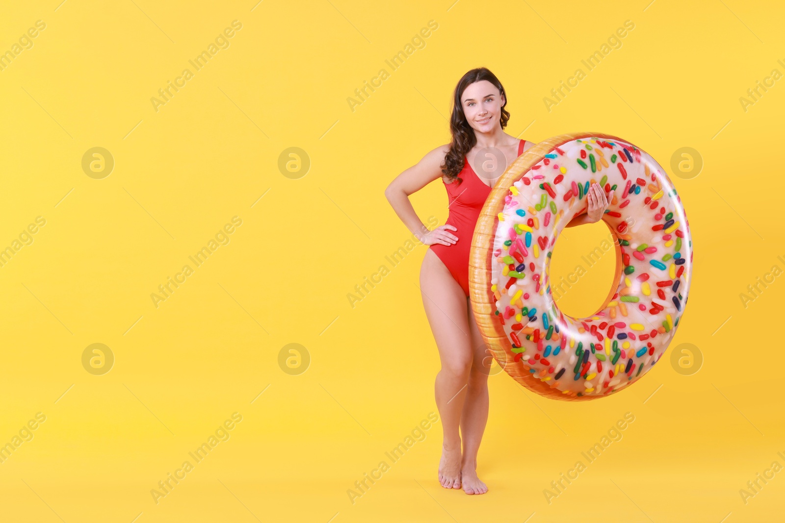 Photo of Beautiful woman in swimsuit with inflatable ring on yellow background. Space for text