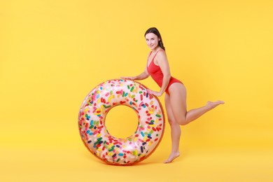 Photo of Beautiful woman in swimsuit with inflatable ring on yellow background