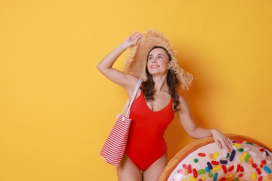 Photo of Beautiful woman wearing swimsuit and straw hat with inflatable ring on yellow background. Space for text