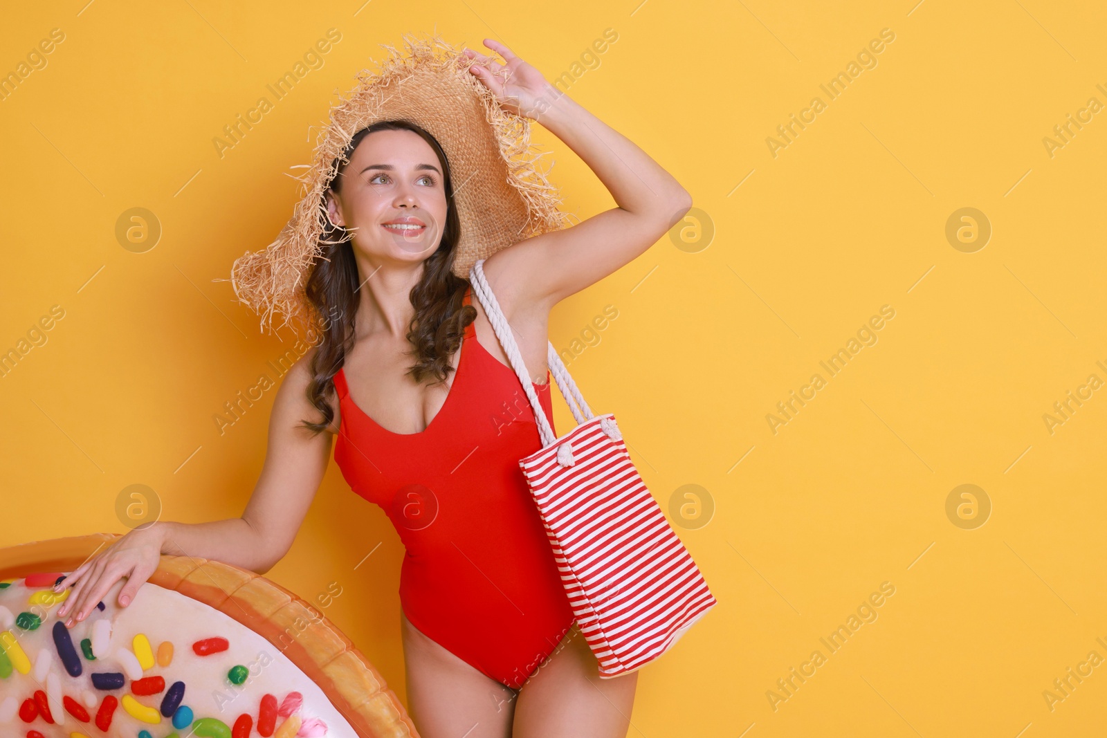 Photo of Beautiful woman wearing swimsuit and straw hat with inflatable ring on yellow background. Space for text