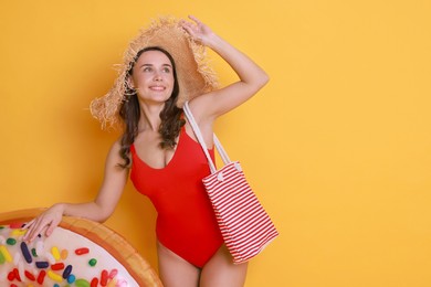 Photo of Beautiful woman wearing swimsuit and straw hat with inflatable ring on yellow background. Space for text