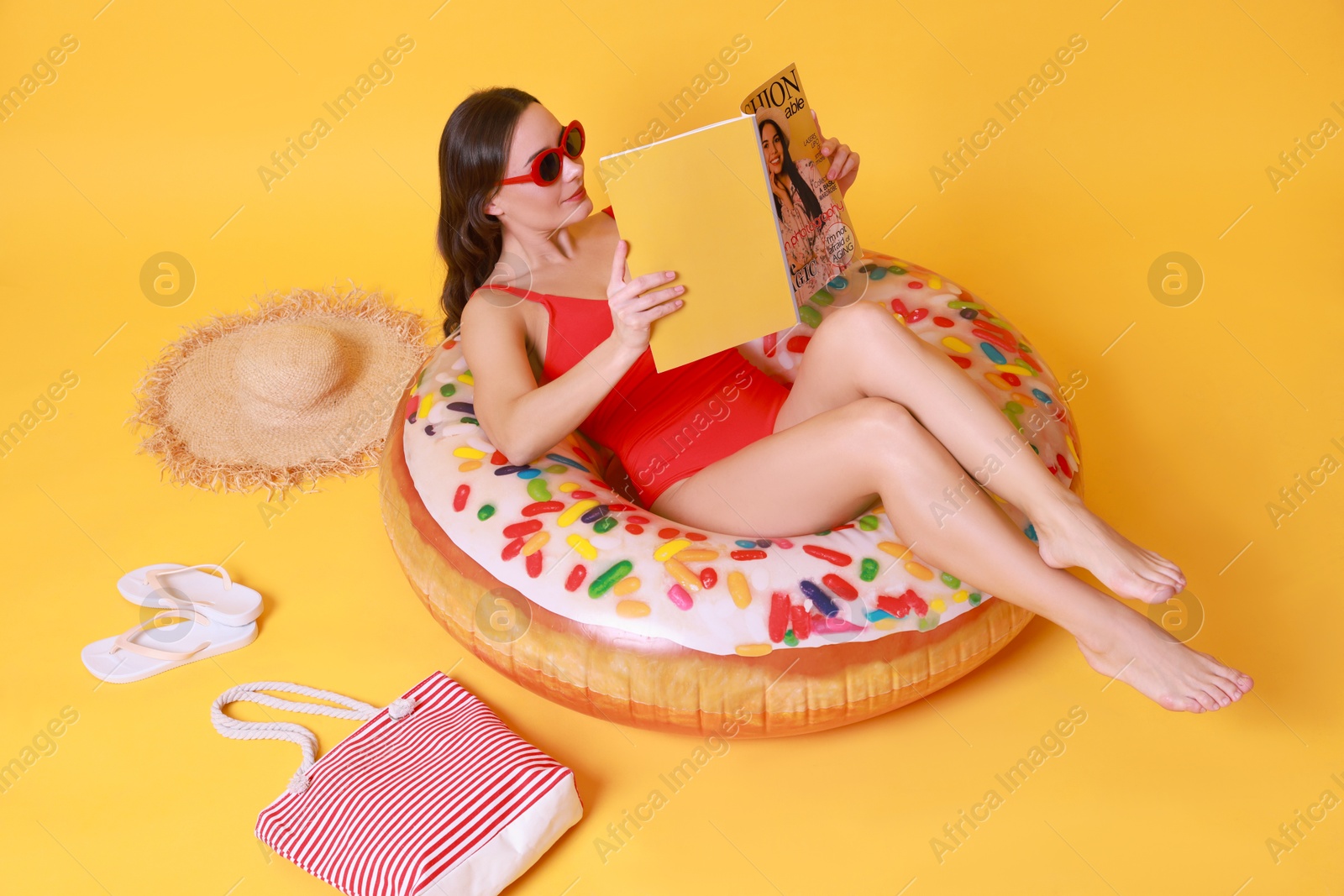 Photo of Beautiful woman with beach accessories reading magazine on yellow background