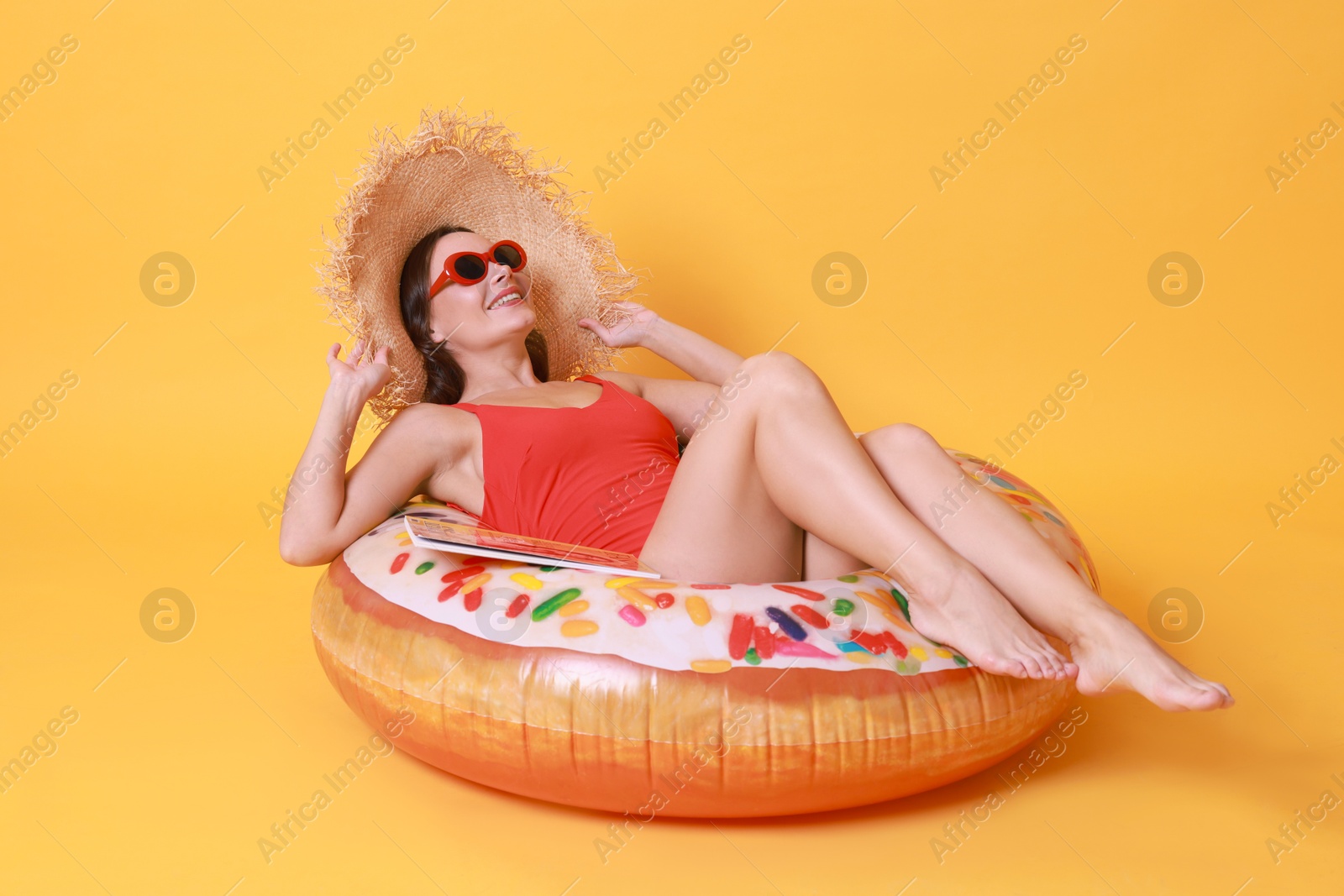 Photo of Beautiful woman wearing swimsuit and straw hat with inflatable ring on yellow background