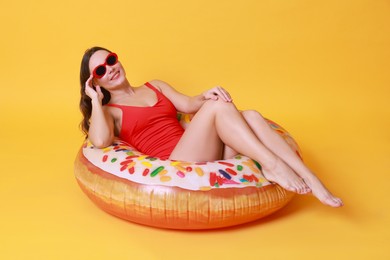 Photo of Beautiful woman in swimsuit with inflatable ring on yellow background