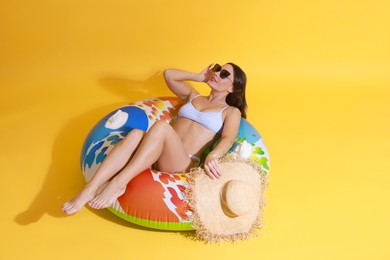 Photo of Beautiful woman in swimsuit with inflatable ring on yellow background