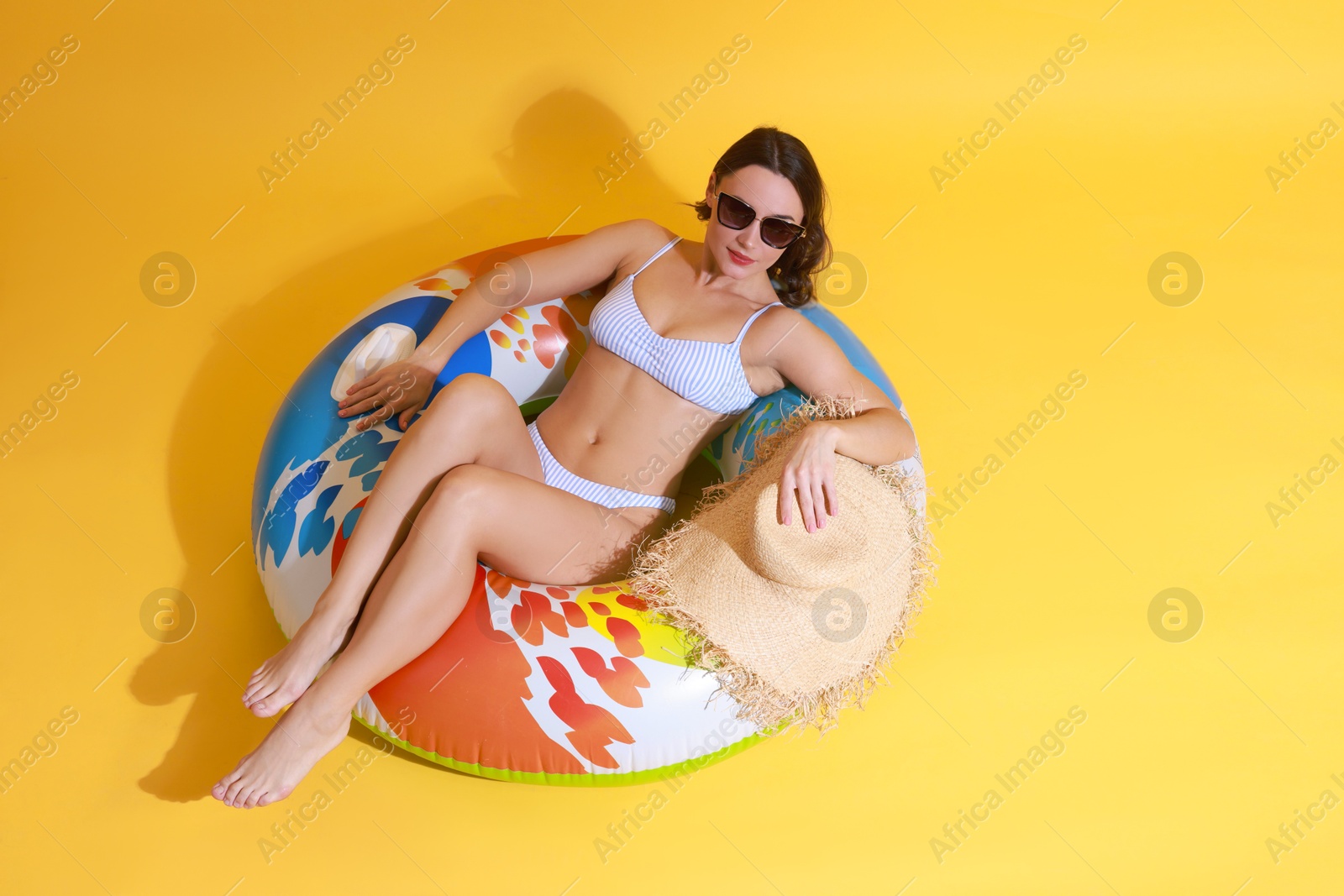 Photo of Beautiful woman in swimsuit with inflatable ring on yellow background