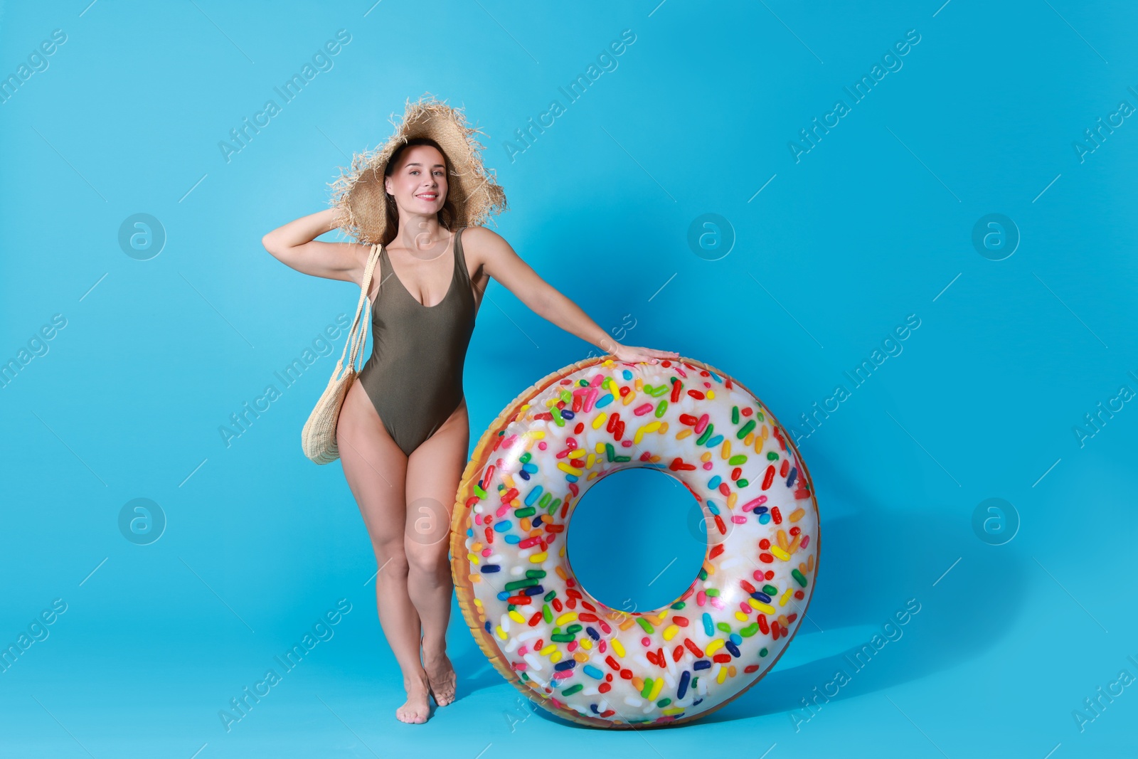 Photo of Beautiful woman wearing swimsuit and straw hat with inflatable ring on light blue background