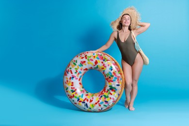 Beautiful woman wearing swimsuit and straw hat with inflatable ring on light blue background